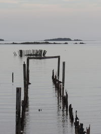 Wooden posts in sea against sky