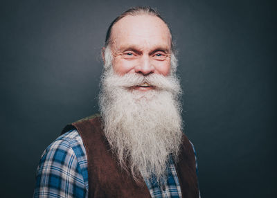 Portrait of smiling senior man with white beard and mustache against gray background