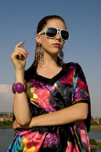 Young woman wearing sunglasses standing against sky