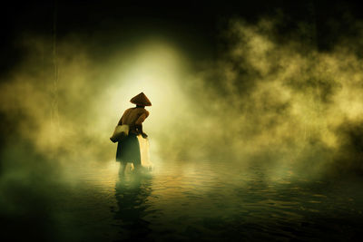 Rear view of fisherman fishing in lake during foggy weather at night