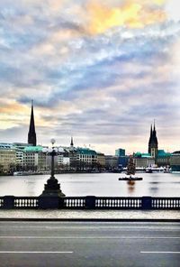 View of city at waterfront against cloudy sky