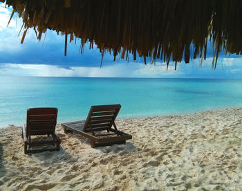 Deck chairs on beach against sky