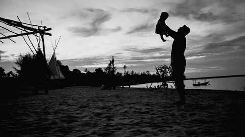 Father holding baby daughter while standing on sand against sea during sunset