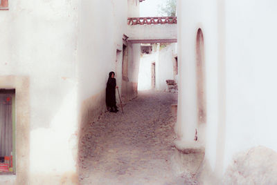 Portrait of senior woman with walking cane standing against wall in city