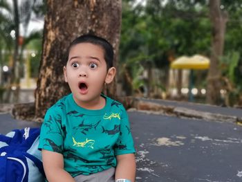 Cute boy with mouth open sitting outdoors