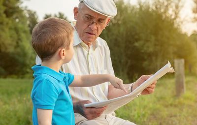 Grandfather reading newspaper while sitting by grandson in park