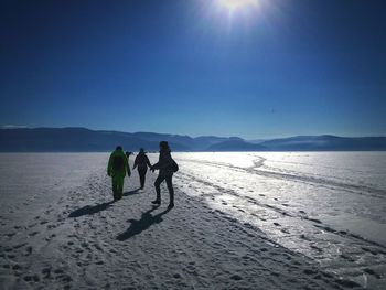People walking on snow covered field against blue sky