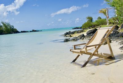 Chair on shore at beach against sky