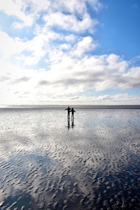 Rear view of men on beach against sky
