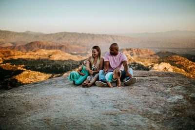 Family of four sitting on a large rock over looking desert city