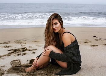 Portrait of beautiful woman sitting on beach against sea