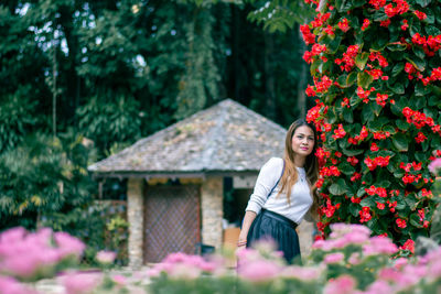 Woman standing by flowering plants against trees