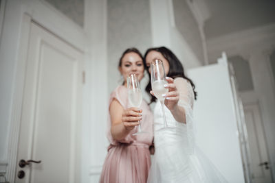 Happy woman holding glass while standing at home