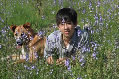 Portrait of boy with dog lying by blooming flowers