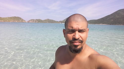 Portrait of shirtless young man in sea against sky