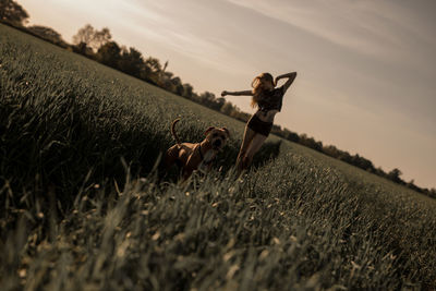 Woman standing with dog on grassy field against sky during sunset