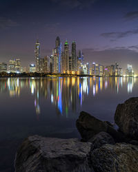 Illuminated buildings by sea against sky at night