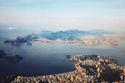 Aerial view of city by sea against sky