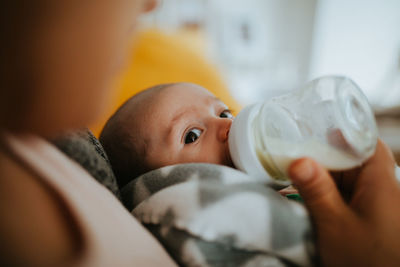 Close-up of mother feeding baby boy while sitting at home