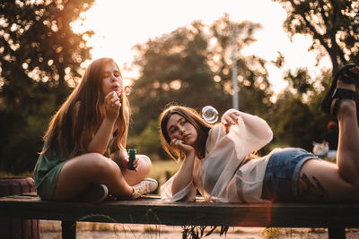 Girlfriends playing with bubbles while relaxing in park in summer