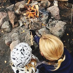 High angle view of mother with daughter roasting sausages over campfire