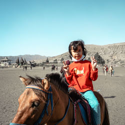 Portrait of young man riding horse in desert against clear sky