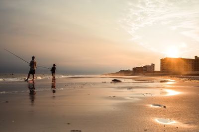 Men standing on beach against sky during sunset