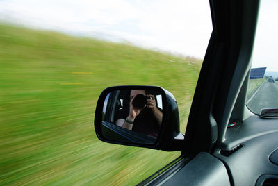 Close-up of woman seen in side-view mirror of car