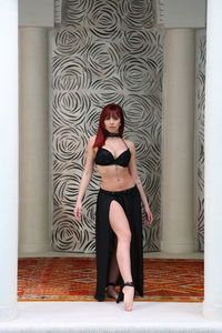 Full length portrait of young woman standing against wall