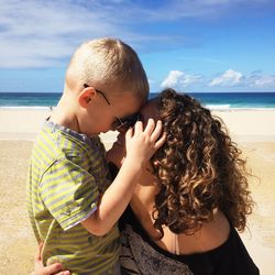 Close-up of happy mother and son on beach against sky