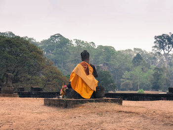 Rear view of man sitting on cross against sky