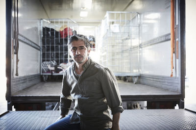 Portrait of mature male volunteer sitting against semi-truck at warehouse