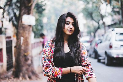 Portrait of young woman standing against tree