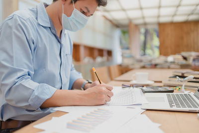 Midsection of wearing mask businessman writing on paper at office