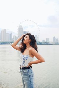 Fashionable young woman standing against sea and urban skyline