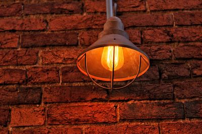 Low angle view of illuminated lamp against brick wall