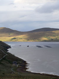 Scenic view of sea by mountain against sky