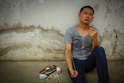 Man holding syringe while sitting against wall