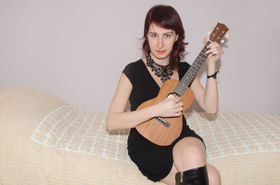 Portrait of woman playing guitar while sitting on bed