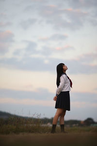 Young woman standing on field against sky