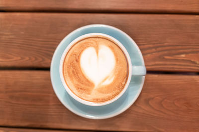 Heart from coffee foam in a blue cup on a wooden table, top view. latte art.