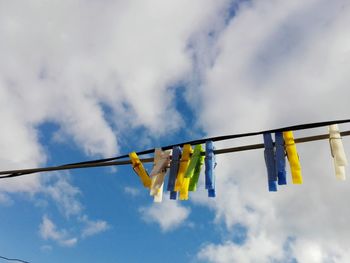 Low angle view of colorful clothespins hanging on clothesline against cloudy sky