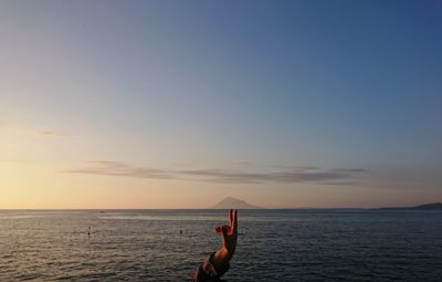 Man surfing in sea against sky during sunset