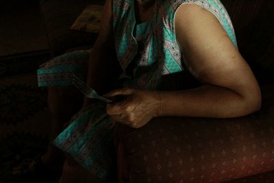 Midsection of woman holding fork while sitting on sofa at home