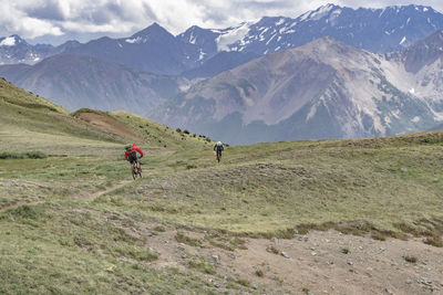 Rear view of men riding bicycle on mountains against sky