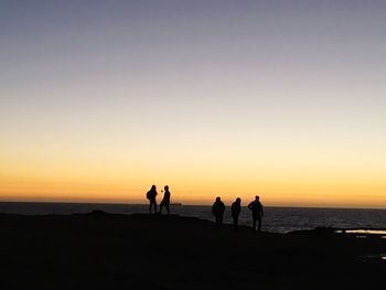 Silhouette friends standing against sea during sunset