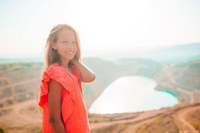 Portrait of smiling young woman standing on land against sky