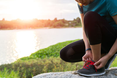 Midsection of man relaxing by lake against sky during sunset