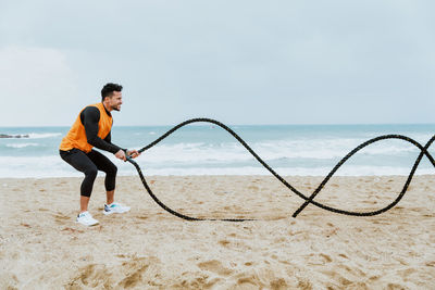 Male athlete exercising with rope at beach