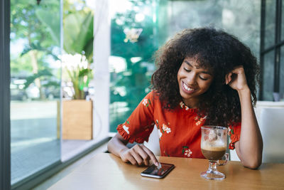 Portrait of smiling young woman in coffee shop using cell phone